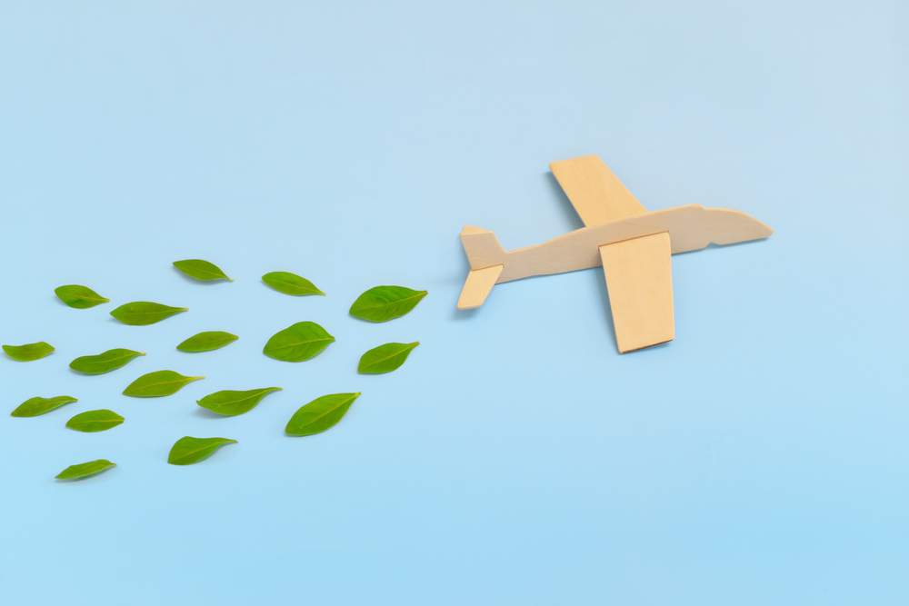 Wooden airplane model emitting fresh green leaves on blue background. Sustainable travel; clean and green energy; and biofuel for aviation industry concept.