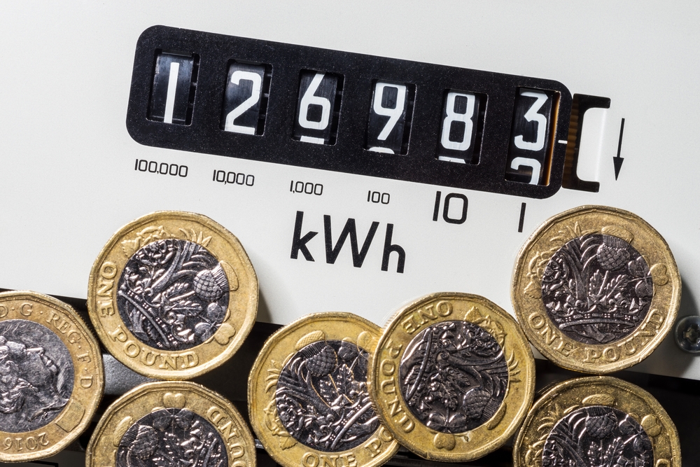 Electricity meter with cash one pound coins. Concept for energy supplier, high bills, price rise, cost of living, inflation, price cap and fuel poverty.