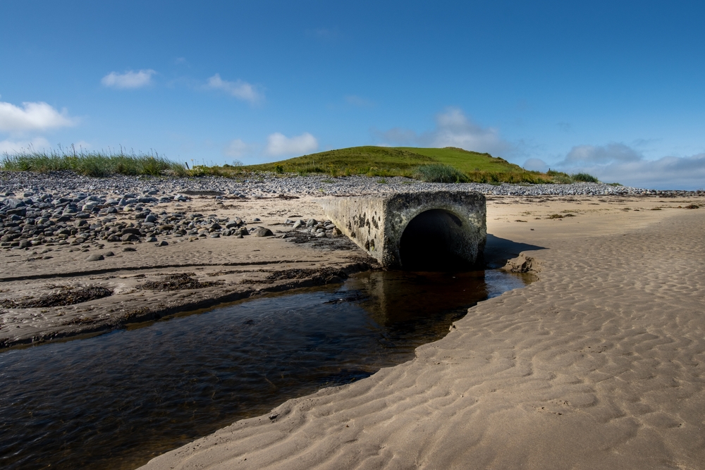 water pollution The outlet pipe for sewage discharges onto a beach