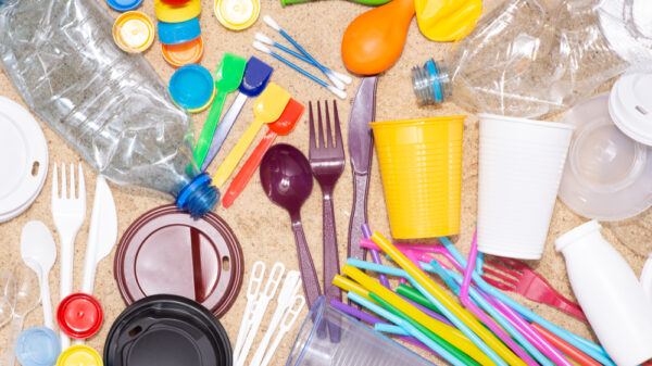 Disposable single-use plastic objects such as bottles, cups, forks, spoons and drinking straws that cause pollution of the environment, especially oceans. Top view on sand