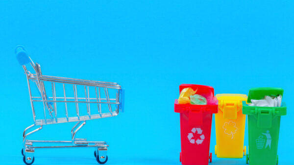 Mini shopping trolley near recycling bins containers on blue background