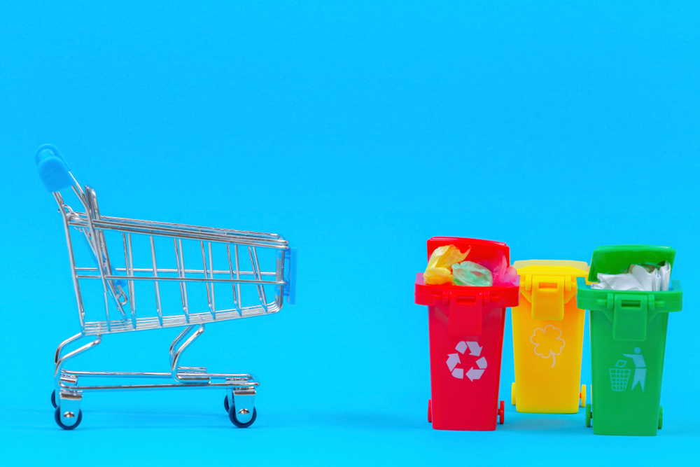 Mini shopping trolley near recycling bins containers on blue background