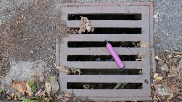 A purple e-cigarette vape has been discarded and left lying on a metal water drain cover.