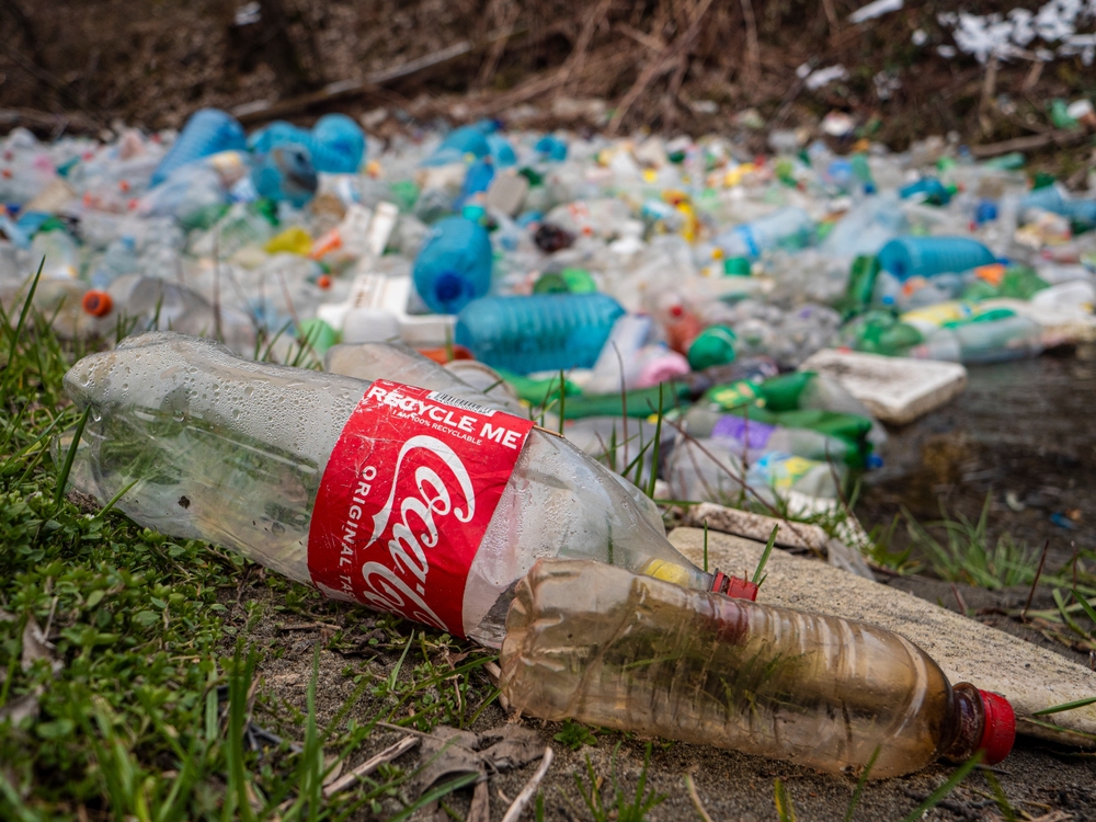 Ironic text on plastic Coca Cola bottle near waste pollution at river. Inappropriate place for garbage disposal. Accumulated plastic garbage floating on the river greenwashing