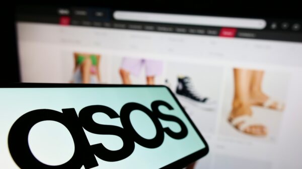 Cellphone with logo of British fashion retail company ASOS plc on screen in front of business website. Focus on center-left of phone display.