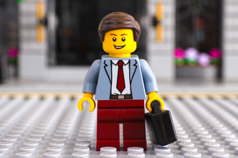Lego businessman with suitcase stay on the street. Studio shot.